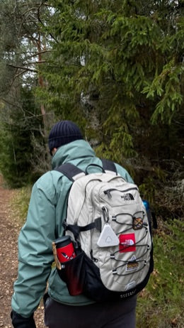Pulse clipped to a hiking pack on a forest trail